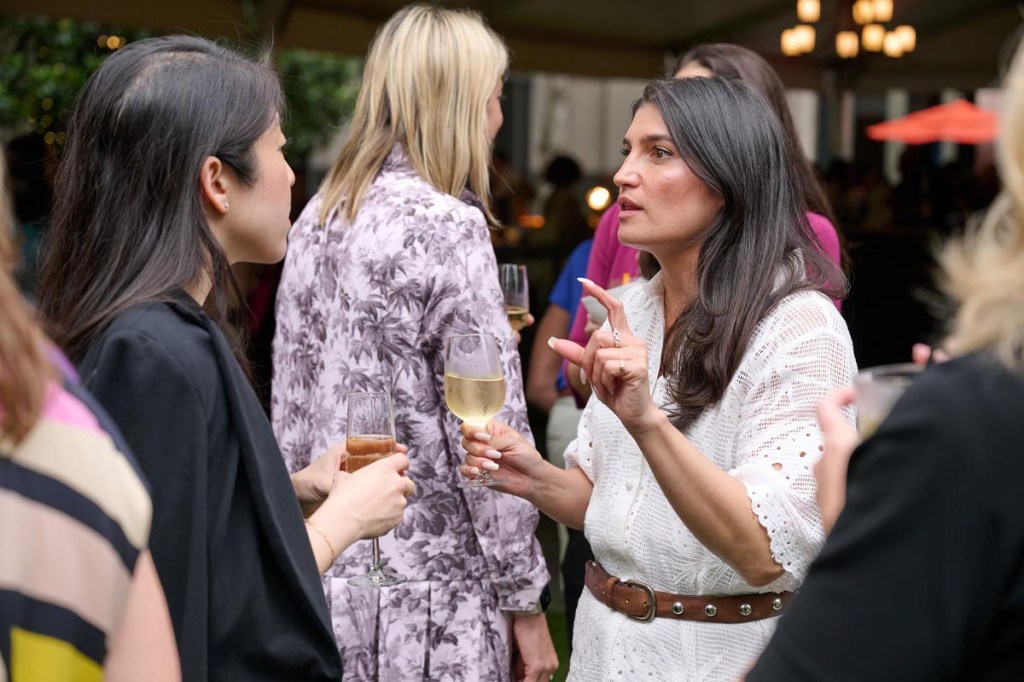 Two women are engaged in a conversation at a Women Leading Travel event, holding wine glasses. The setting is lively, with a relaxed, convivial atmosphere.